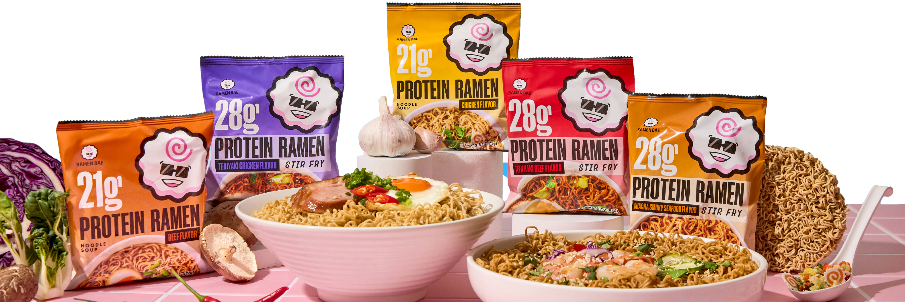 Packages of Protein Ramen with bowls of noodles and garnishes on a pink background