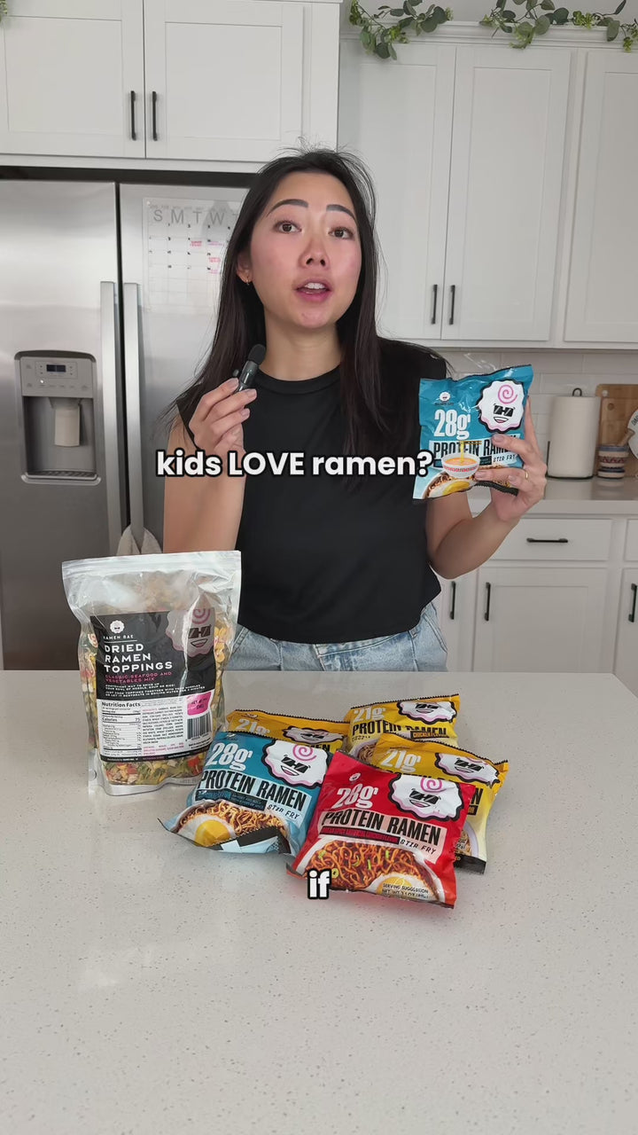 Woman holds Ramen Bae Protein Ramen and topping packages in a kitchen, then stirs cooked noodles with vegetables into a bowl